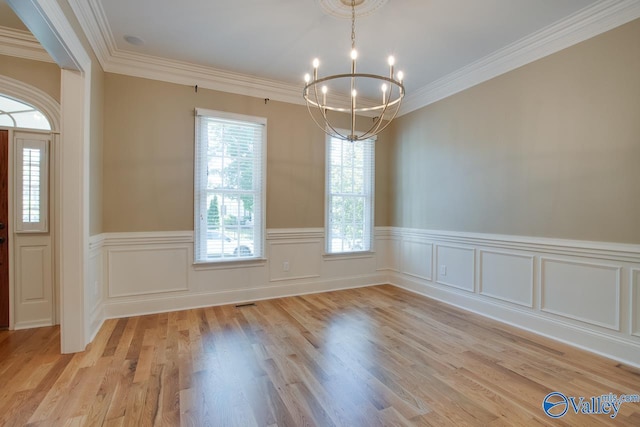 unfurnished dining area with ornamental molding, light wood-style floors, a wainscoted wall, and an inviting chandelier