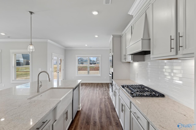 kitchen featuring stainless steel appliances, light stone countertops, custom range hood, pendant lighting, and sink