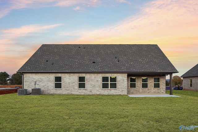 back house at dusk featuring a patio, a yard, and central AC unit