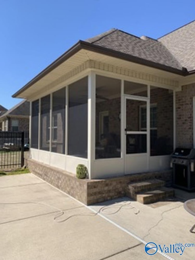 view of side of home with a patio, brick siding, fence, and a sunroom