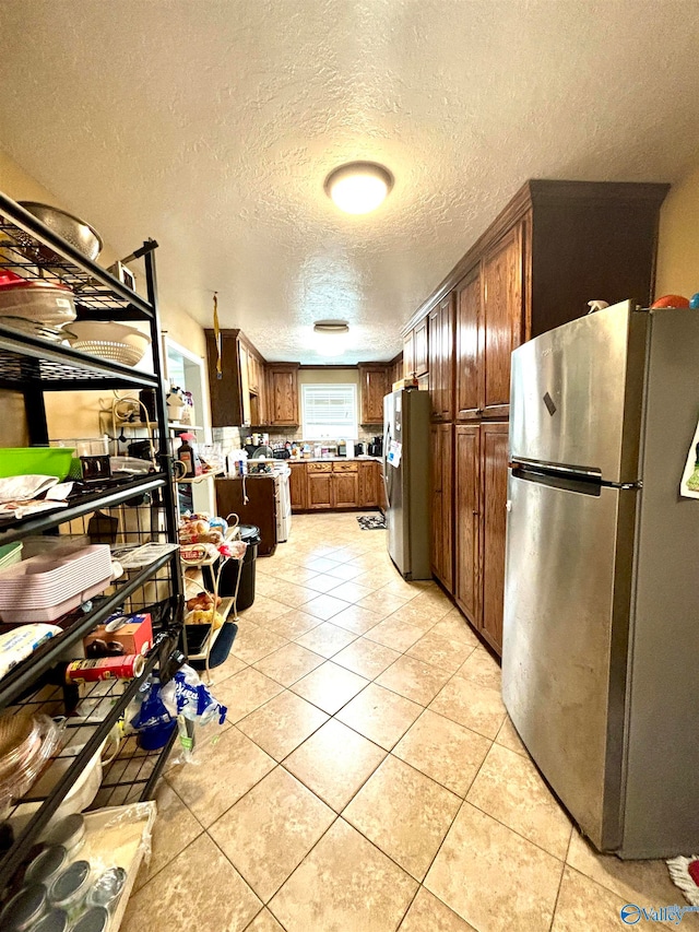 kitchen featuring tasteful backsplash, a textured ceiling, light tile patterned floors, and stainless steel refrigerator