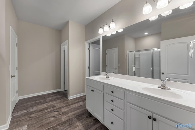 bathroom featuring double vanity, a shower stall, wood finished floors, and a sink