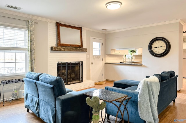 living room featuring crown molding, plenty of natural light, a fireplace, and light wood-type flooring