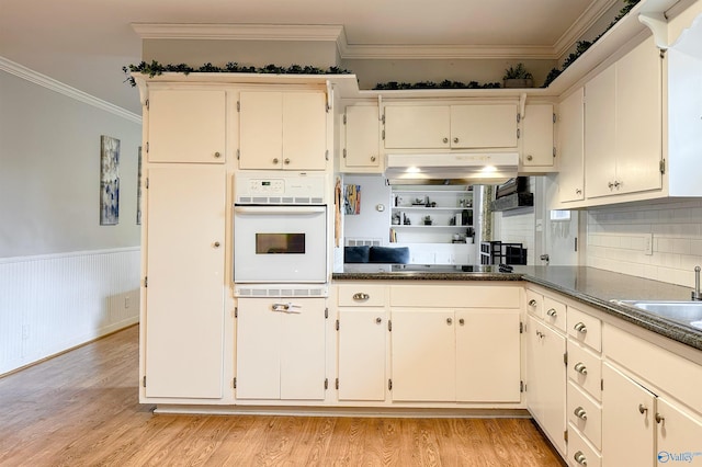 kitchen with sink, ornamental molding, oven, and light wood-type flooring