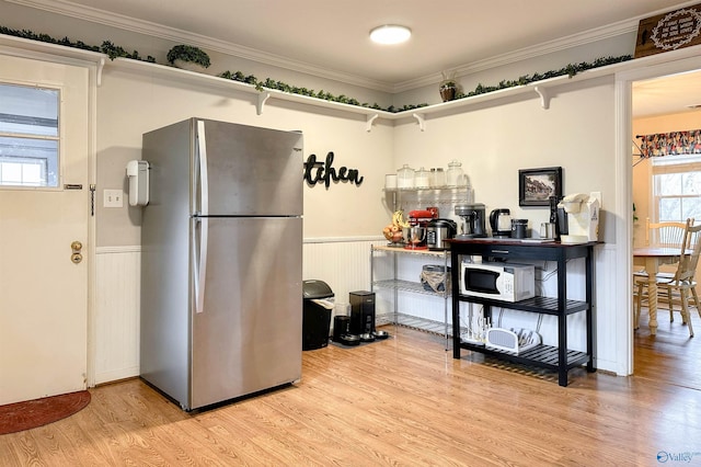 kitchen with light hardwood / wood-style flooring, ornamental molding, and stainless steel refrigerator