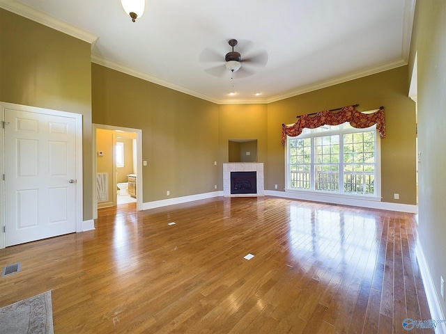 unfurnished living room featuring a tiled fireplace, ceiling fan, hardwood / wood-style flooring, and crown molding