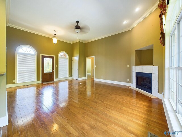 unfurnished living room with a tile fireplace, light hardwood / wood-style floors, ornamental molding, and ceiling fan