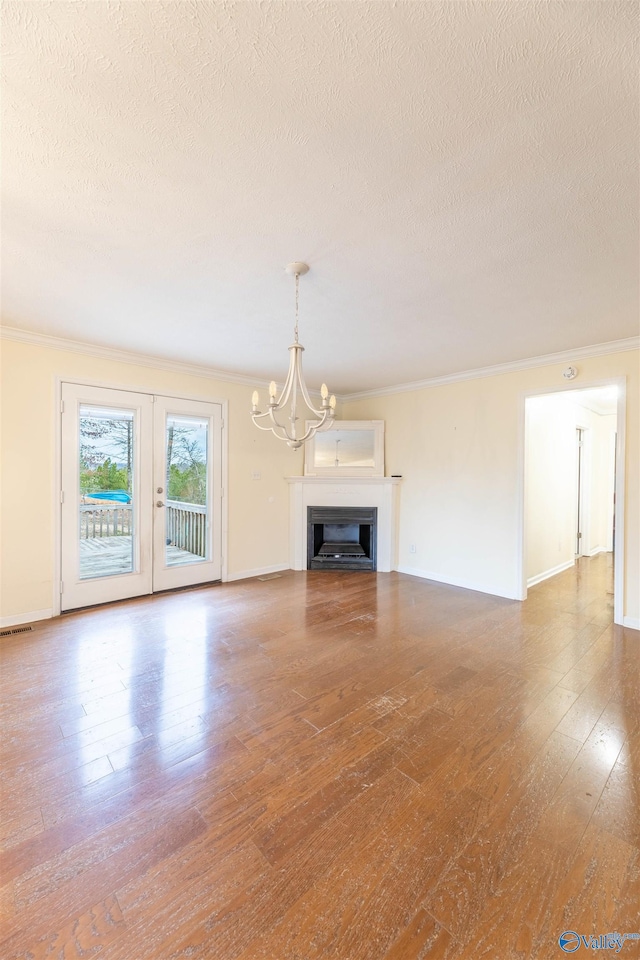 unfurnished living room with wood-type flooring, ornamental molding, a textured ceiling, french doors, and a chandelier