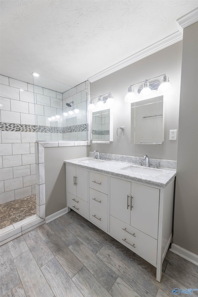 bathroom featuring a textured ceiling, double vanity, walk in shower, and a sink