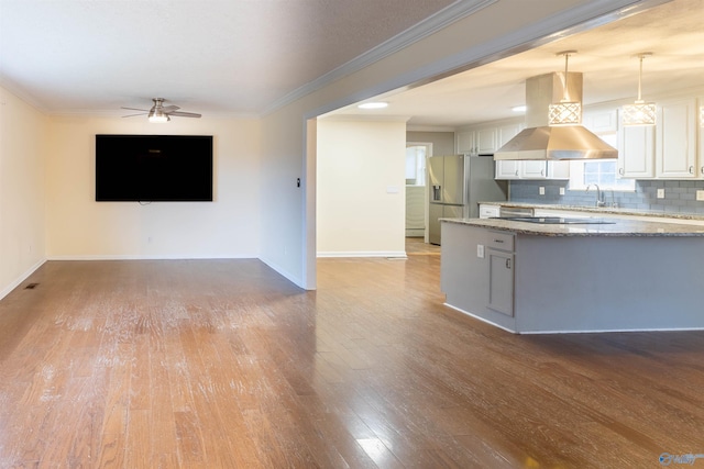 kitchen with light stone counters, stainless steel refrigerator with ice dispenser, light wood finished floors, backsplash, and island range hood