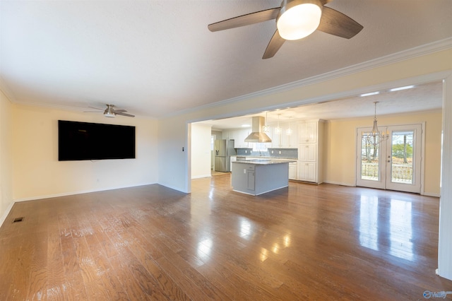 unfurnished living room featuring baseboards, visible vents, ornamental molding, wood finished floors, and ceiling fan with notable chandelier