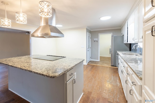 kitchen with black electric stovetop, island range hood, a sink, ornamental molding, and light wood finished floors