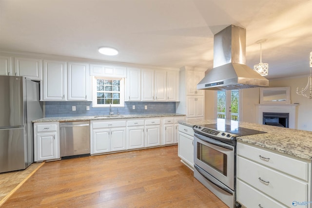 kitchen with light wood finished floors, decorative backsplash, appliances with stainless steel finishes, a sink, and island range hood