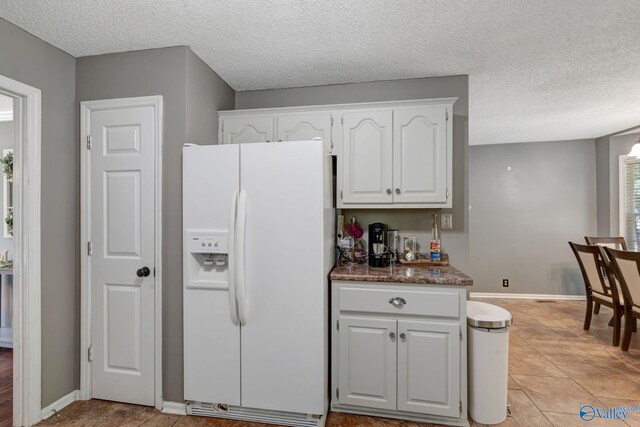 kitchen featuring white fridge with ice dispenser, light tile patterned floors, a textured ceiling, and white cabinets