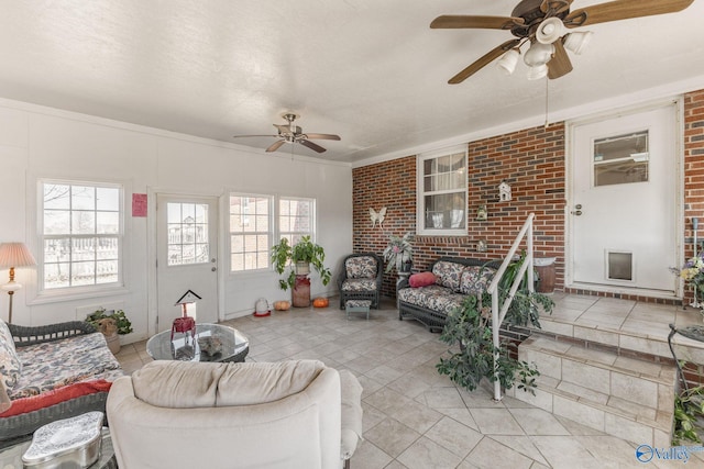 living room with ceiling fan, ornamental molding, brick wall, and a textured ceiling