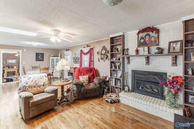 living room featuring ceiling fan, a brick fireplace, hardwood / wood-style floors, and a textured ceiling