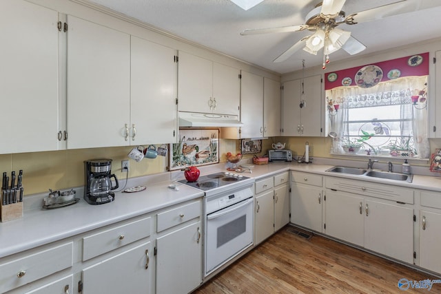 kitchen with light countertops, a sink, light wood-style flooring, under cabinet range hood, and electric stove