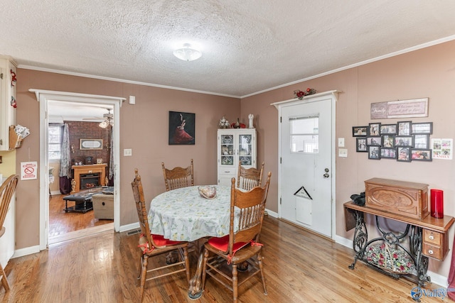 dining area featuring a textured ceiling, light wood-type flooring, ornamental molding, brick wall, and a fireplace