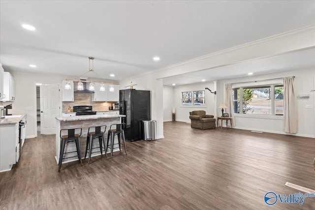 kitchen with black appliances, a center island, wall chimney exhaust hood, light countertops, and decorative backsplash