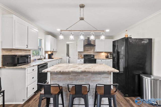 kitchen with black appliances, wall chimney range hood, white cabinets, and a sink