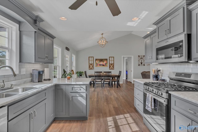 kitchen with gray cabinetry, stainless steel appliances, lofted ceiling, and sink