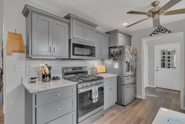 kitchen with light wood-type flooring, tasteful backsplash, gray cabinetry, stainless steel appliances, and ceiling fan