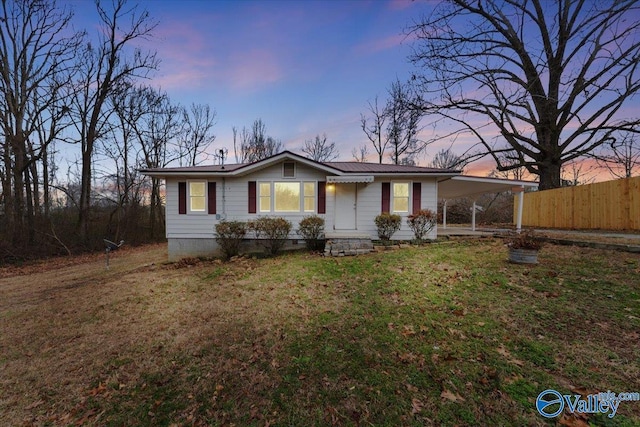 view of front facade featuring an attached carport, fence, a lawn, and metal roof