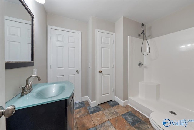 full bath featuring stone tile floors, vanity, a shower, and baseboards