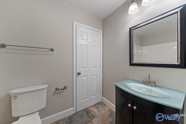 bathroom with vanity, toilet, baseboards, and stone finish flooring