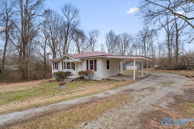 view of front facade featuring a carport, driveway, metal roof, and an outbuilding