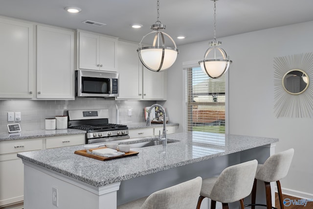 kitchen featuring appliances with stainless steel finishes, tasteful backsplash, white cabinetry, and an island with sink