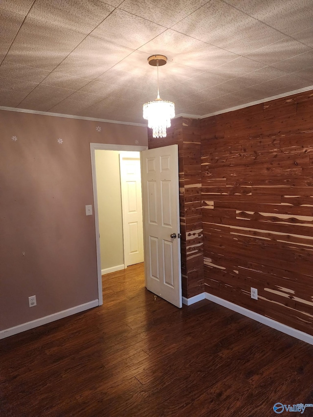 unfurnished room featuring crown molding, dark hardwood / wood-style floors, a chandelier, and wood walls