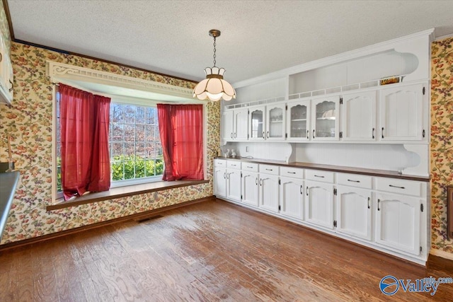 kitchen featuring dark hardwood / wood-style floors, crown molding, a textured ceiling, decorative light fixtures, and white cabinets