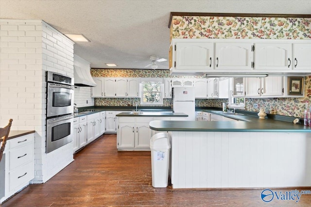 kitchen featuring white cabinets, a textured ceiling, double oven, white fridge, and custom range hood