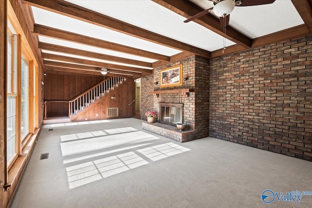 unfurnished living room featuring beam ceiling, ceiling fan, wooden walls, a fireplace, and carpet