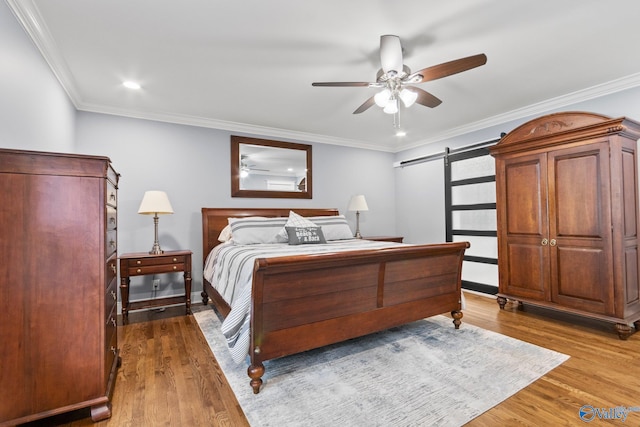 bedroom with a barn door, hardwood / wood-style floors, ceiling fan, and crown molding