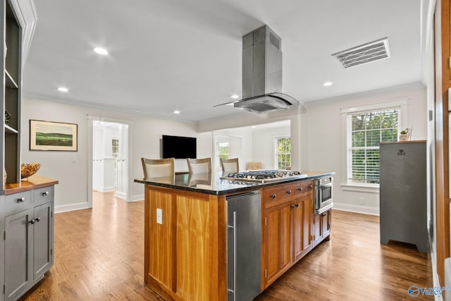 kitchen featuring a kitchen island, light hardwood / wood-style flooring, island range hood, ornamental molding, and dark stone countertops