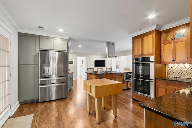 kitchen with dark stone countertops, hardwood / wood-style floors, backsplash, stainless steel appliances, and island exhaust hood