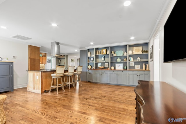 kitchen with light hardwood / wood-style floors, gray cabinets, island exhaust hood, a breakfast bar, and ornamental molding