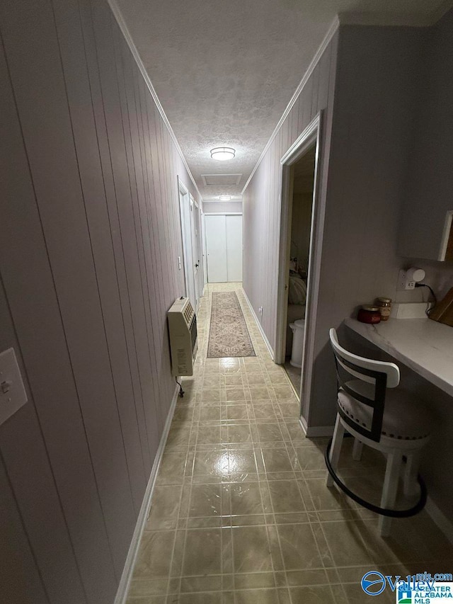 corridor with a textured ceiling, heating unit, crown molding, wooden walls, and tile patterned flooring