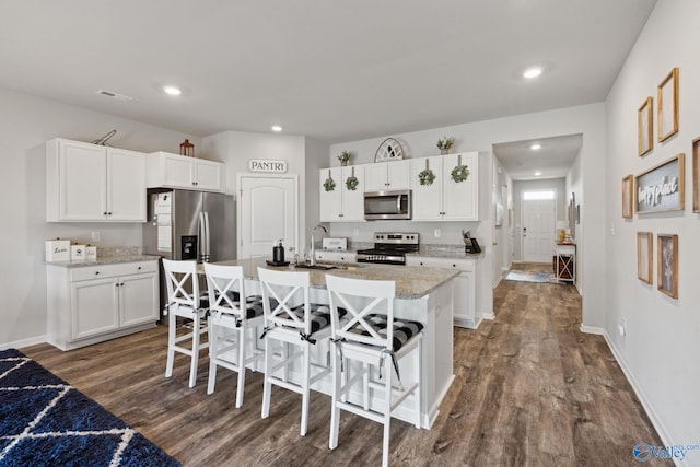 kitchen featuring a breakfast bar area, white cabinets, an island with sink, and appliances with stainless steel finishes