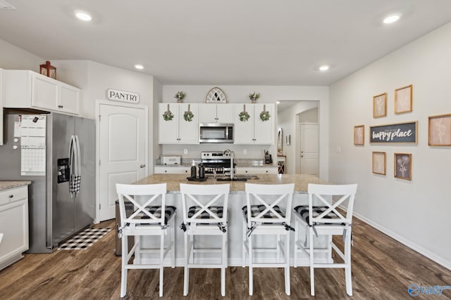 kitchen featuring a center island with sink, appliances with stainless steel finishes, a kitchen bar, sink, and white cabinetry