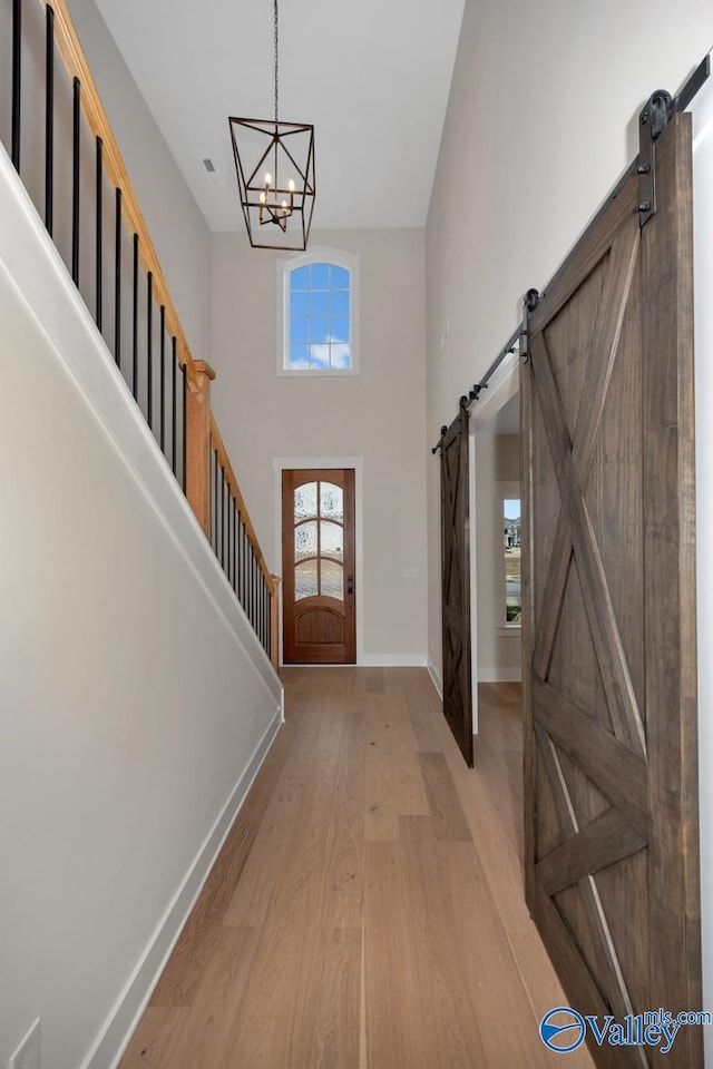 foyer entrance with a barn door, a towering ceiling, baseboards, stairs, and light wood-type flooring