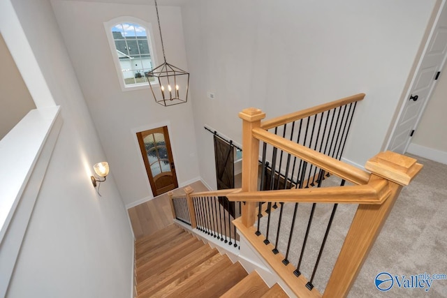 stairs with a high ceiling, baseboards, a notable chandelier, and wood finished floors