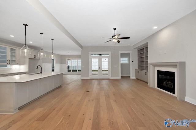 unfurnished living room with light wood-style flooring, built in features, baseboards, and a glass covered fireplace