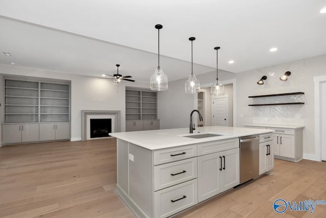 kitchen featuring a center island with sink, a fireplace, stainless steel dishwasher, light wood-style floors, and a sink