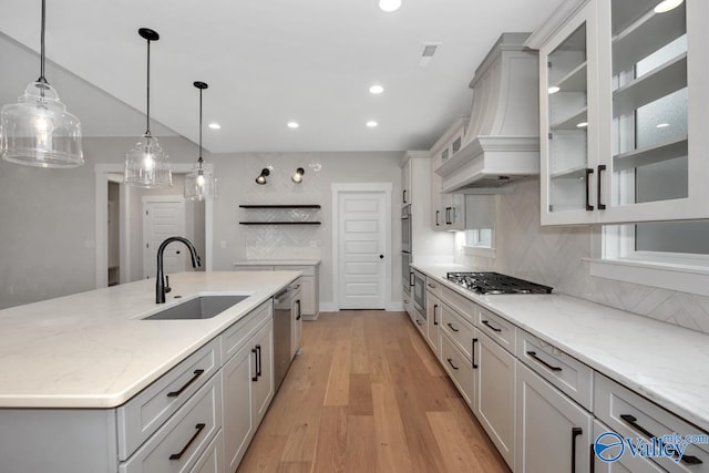 kitchen featuring a sink, light wood-style floors, appliances with stainless steel finishes, custom exhaust hood, and tasteful backsplash