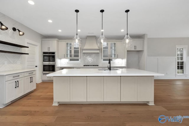 kitchen featuring stainless steel double oven, premium range hood, a sink, open shelves, and cooktop