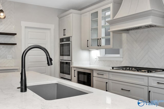 kitchen with a sink, appliances with stainless steel finishes, open shelves, tasteful backsplash, and custom range hood