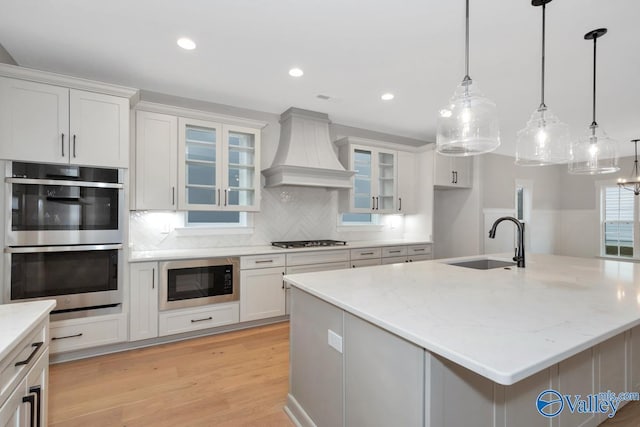 kitchen with custom range hood, built in microwave, double oven, gas cooktop, and a sink